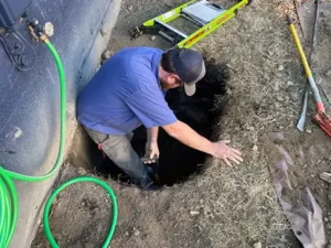 A plumber from Apollo Plumbing working on a sewer line repair in Everett, WA, standing in a dug hole with tools and a garden hose nearby.