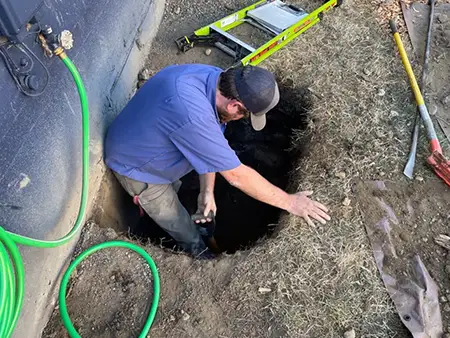 A plumber from Apollo Plumbing working on a sewer line repair in Everett, WA, standing in a dug hole with tools and a garden hose nearby.