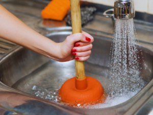 Woman trying to unclog kitchen drain with plunger