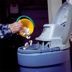 Homeowner adding salt pellets to a water softener system for regular maintenance.